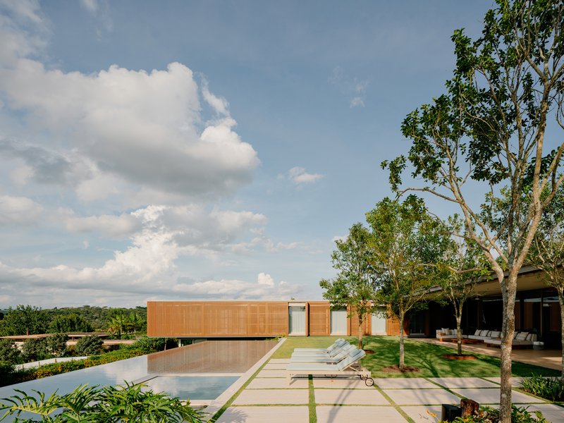 Pool deck with chaise lounges, grass pavers, and timber-clad pavilion under partly cloudy sky