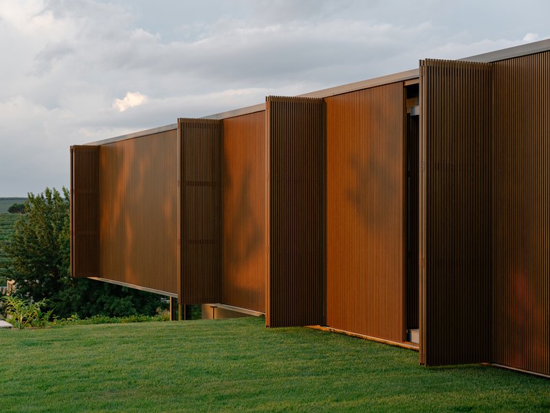 Weathered copper facade with alternating flat and corrugated panels on a grassy slope