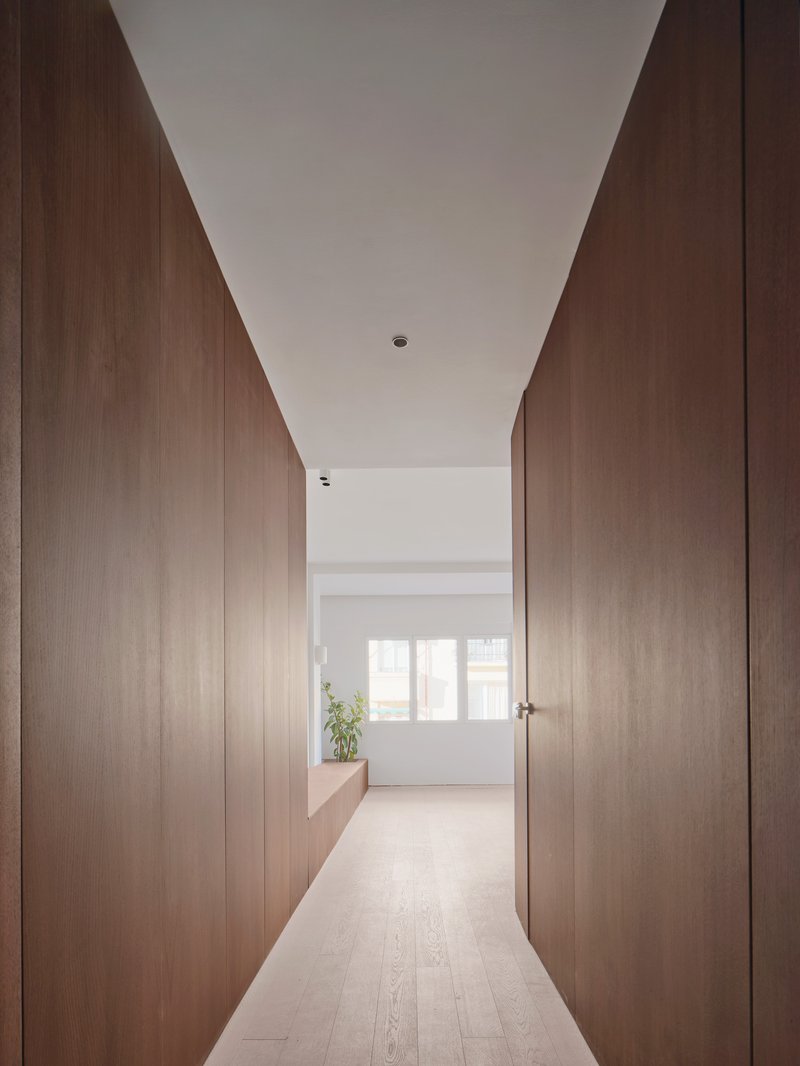 Hallway with walnut-clad walls and pale oak flooring leading to a sunlit room ahead