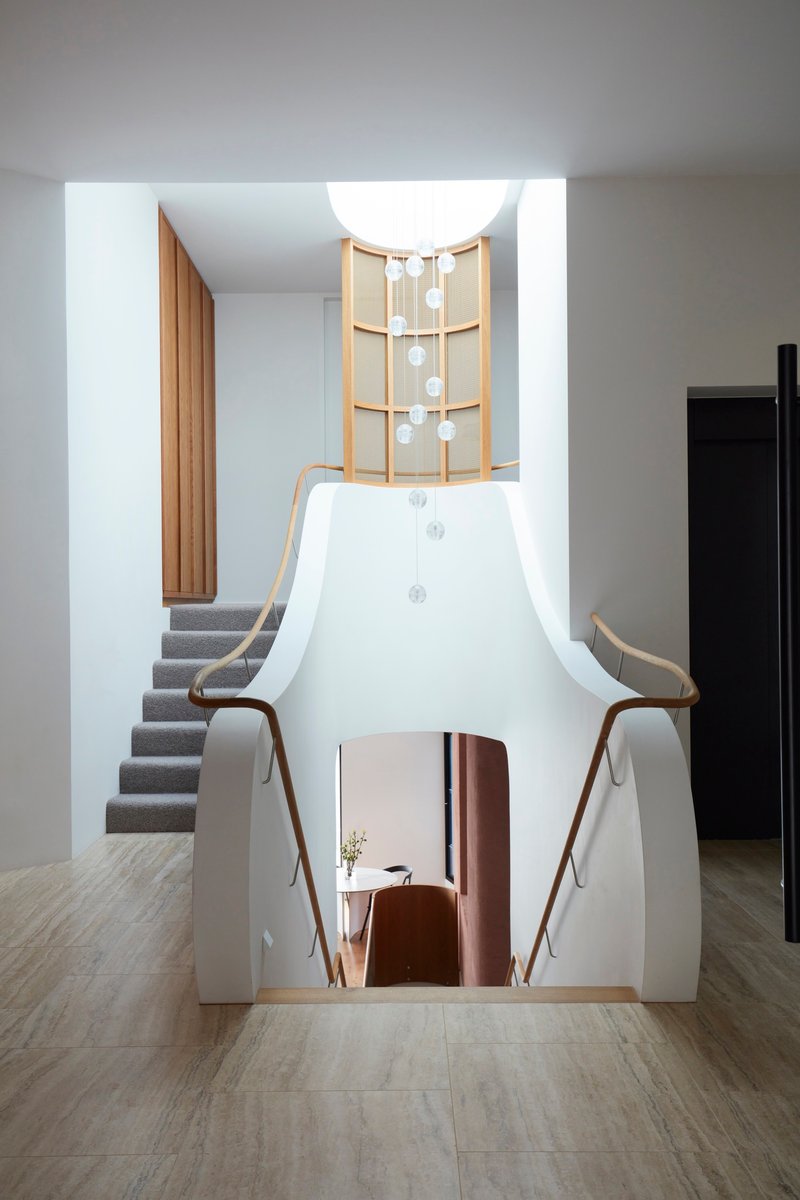 White sculptural stair volume with timber shelving and descending pendant lights under skylight