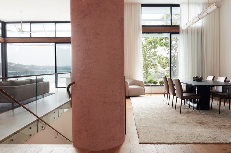 Cylindrical rammed earth column anchoring dining area with harbor views through floor-to-ceiling windows