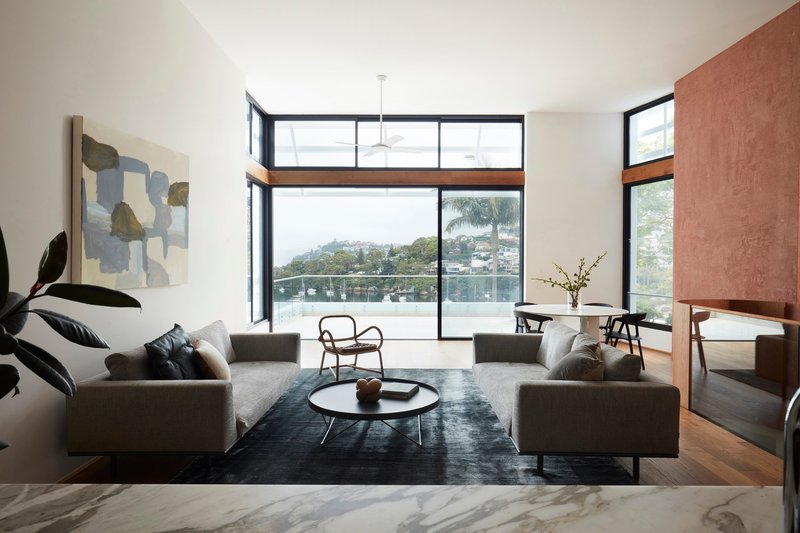 Living room overlooking water with black-framed glazing and rammed earth wall dividing adjacent spaces