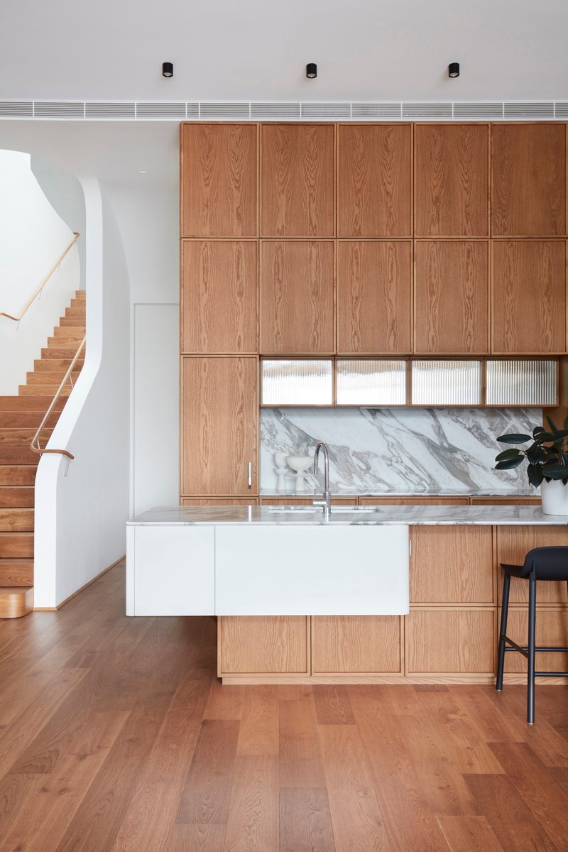 Kitchen with floor-to-ceiling oak veneer cabinetry and marble backsplash beside the timber staircase