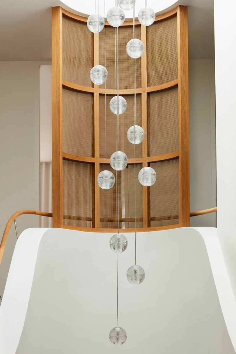 Cascading glass pendant lights in the curved stairwell with oak-framed woven cane screens