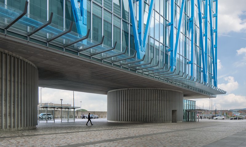 Underside of the cantilevered volume with vertical concrete fins and a pedestrian crossing the plaza