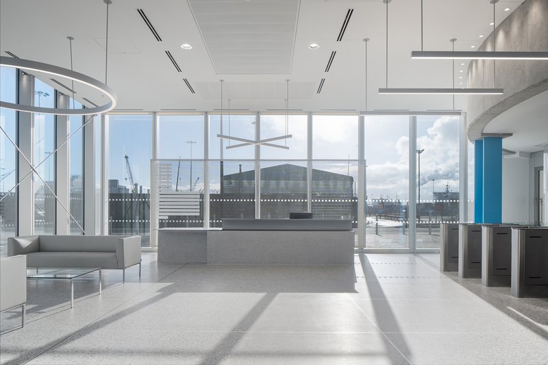 Interior lobby with floor-to-ceiling glazing, suspended linear lighting and a polished stone floor