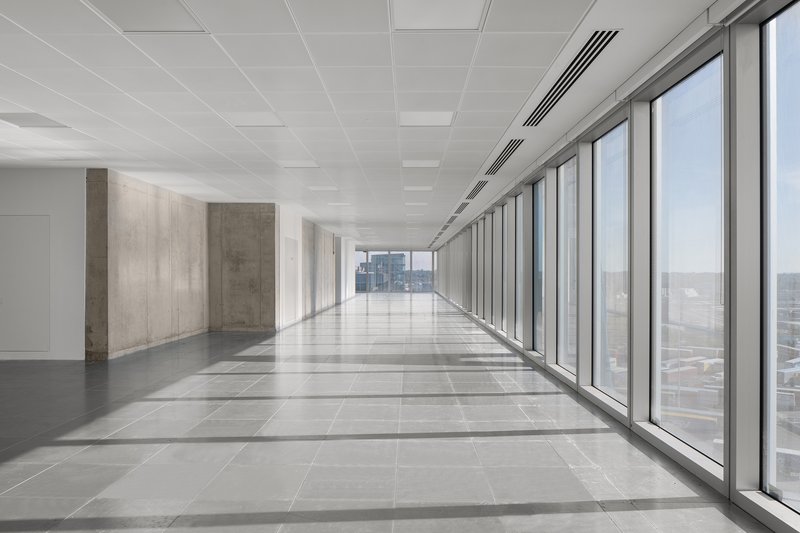 Long corridor with floor-to-ceiling windows along one side and concrete wall panels on the other