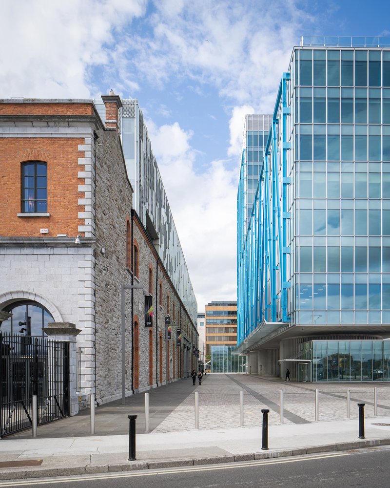 Street view showing stone warehouse facade alongside glass tower with diagonal blue steel exoskeleton