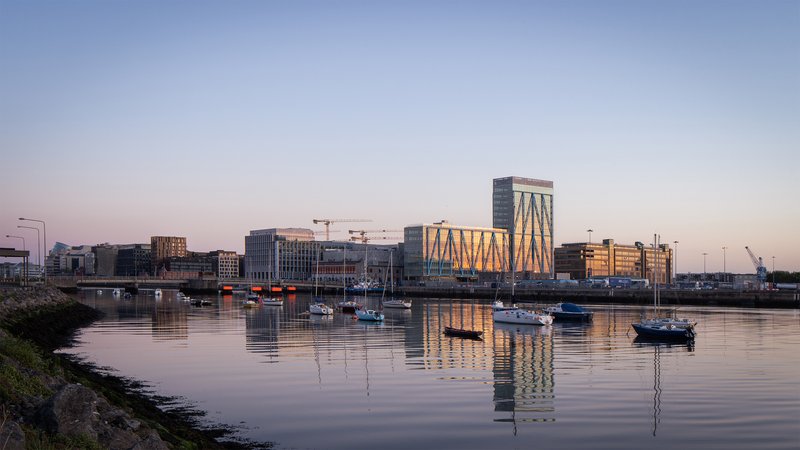 Waterfront view of the diagonal-braced tower reflected in the calm harbor at sunset with moored boats