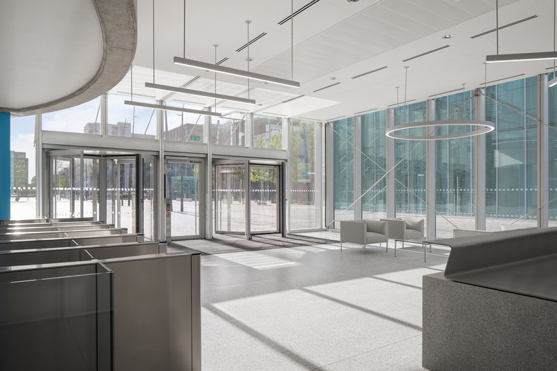 Ground floor lobby with glass revolving doors and pendant light fixtures filtering daylight onto terrazzo flooring