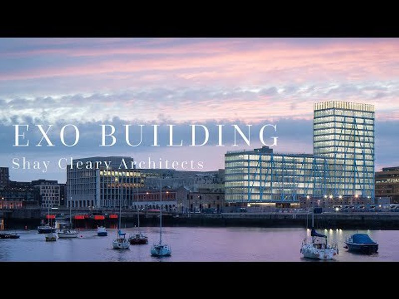 Glass and steel tower rising above a waterfront with moored sailboats at dusk