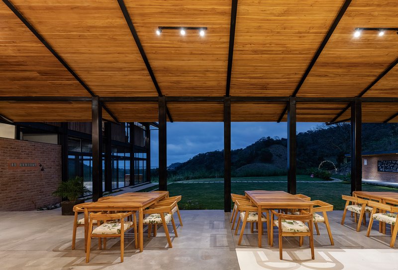 Open-air dining terrace with timber ceiling panels and steel beams overlooking hills at dusk