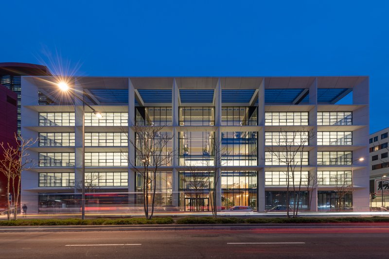 Front facade at twilight with illuminated glazing framed by deep concrete beams and bare trees