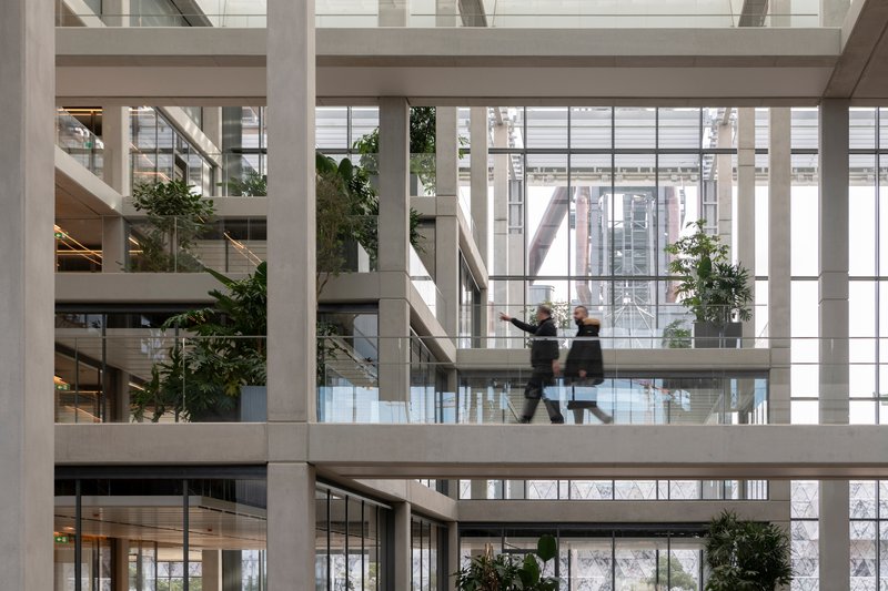 Atrium walkway with two figures in motion and greenery on tiered levels