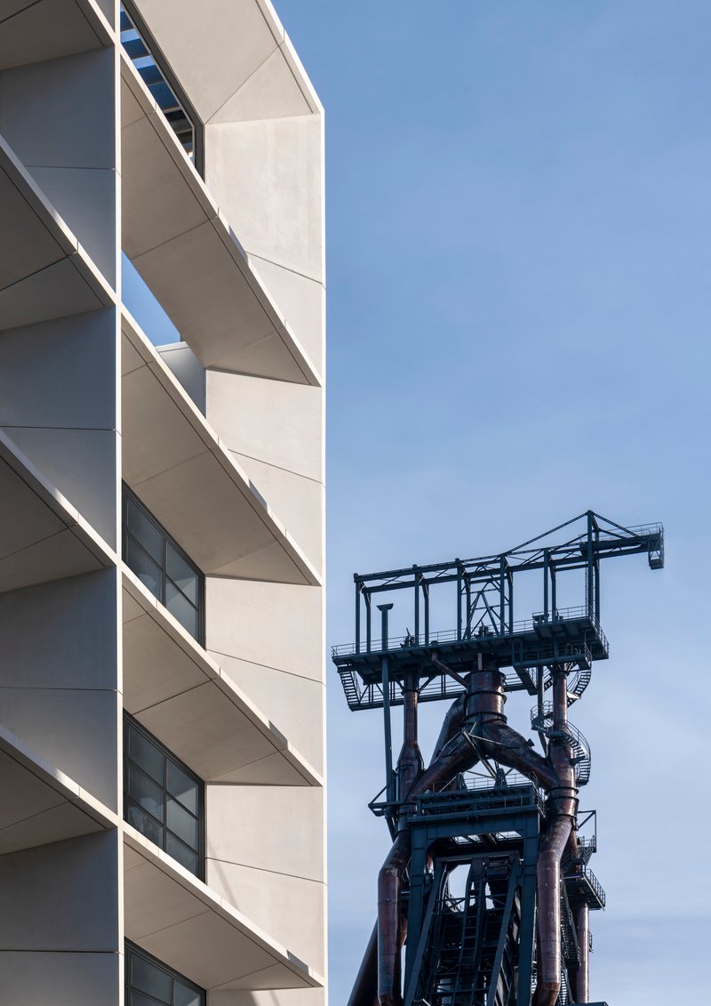 Facade detail with recessed balconies beside a black steel mining headframe structure