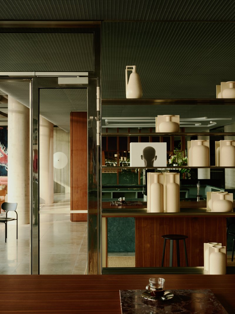 Interior view through open glass doors showing shelving unit with ceramic vessels and green grooved ceiling above