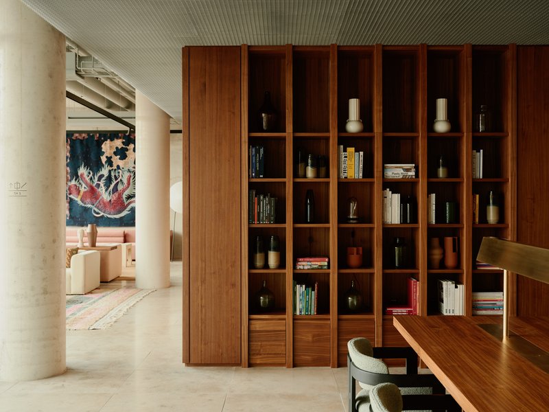 Floor-to-ceiling wooden bookcase dividing dining area from living room with artwork visible beyond cylindrical columns