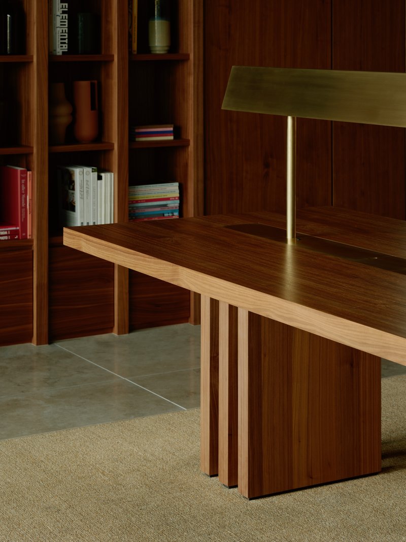 Close-up of timber table with brass lamp and slatted base beside walnut shelving unit