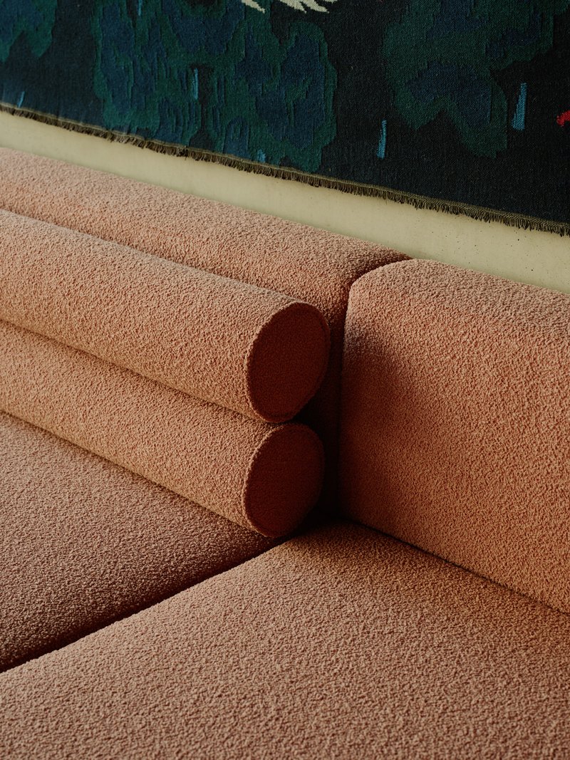 Close-up of a pink textured sofa with cylindrical cushion against a deep blue tapestry