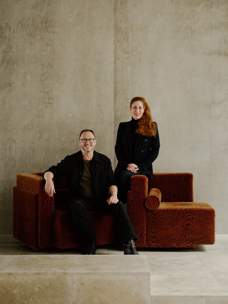 Two people seated on an orange corduroy modular sofa before a concrete wall