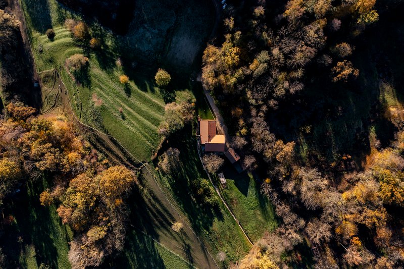 Aerial view of the tiled roof compound nestled between meadows and autumn woodland with long shadows