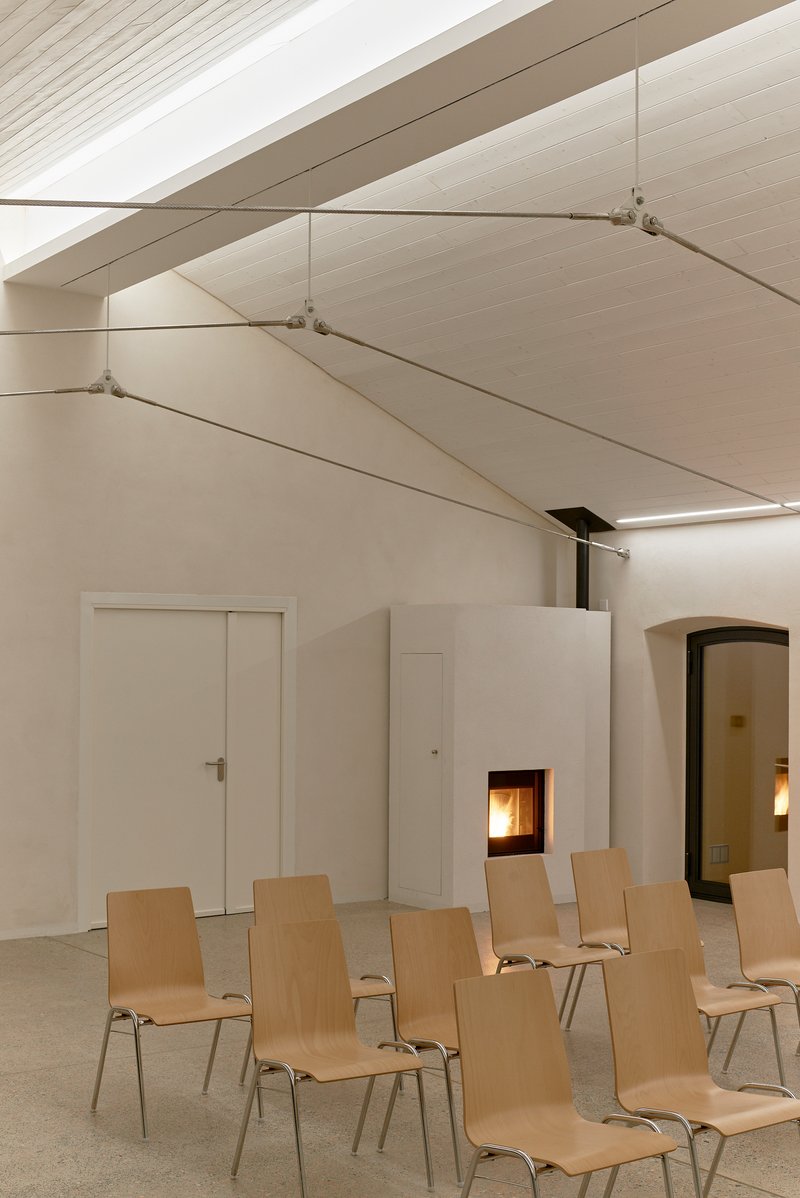 Vaulted ceiling with tensioned fabric panels and cable supports above rows of plywood chairs and fireplace insert
