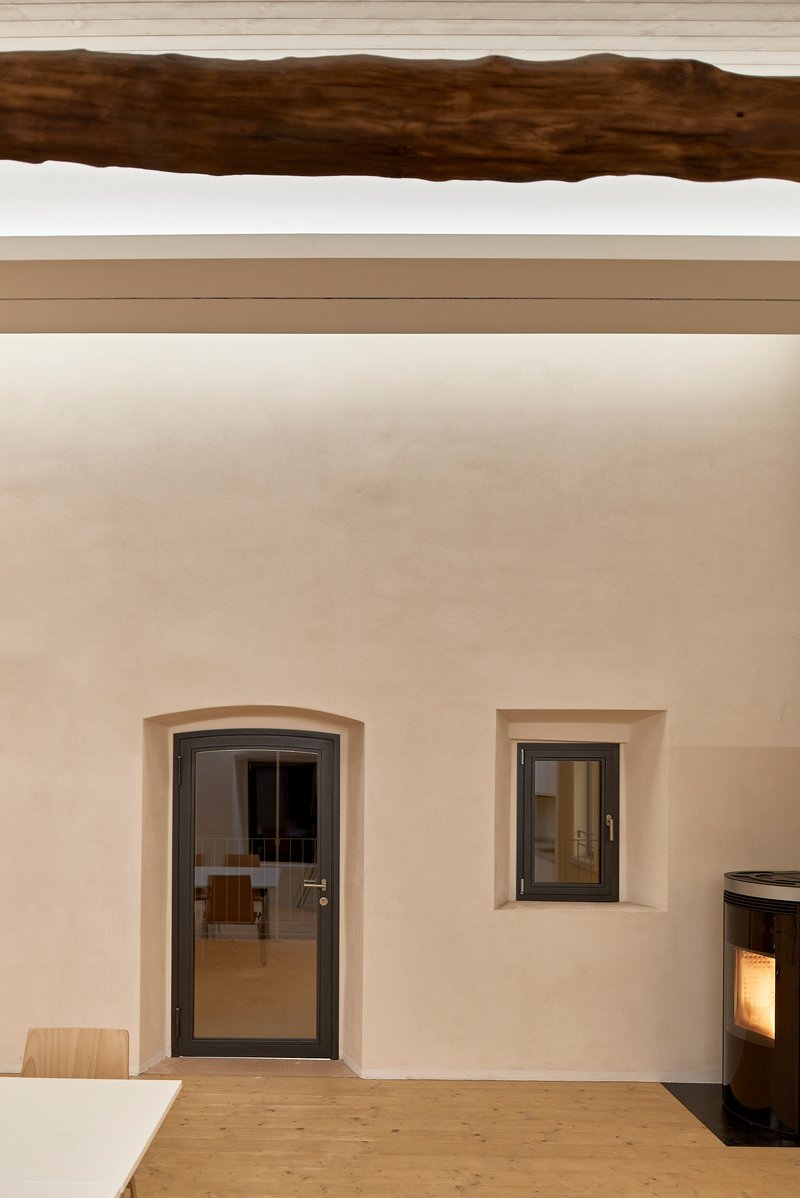 Interior wall with arched doorway, square window opening, exposed timber beam overhead, and pellet stove