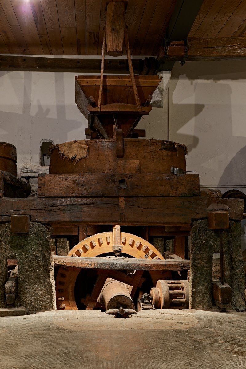 Historic wooden mill machinery with timber gears and hopper beneath exposed ceiling joists