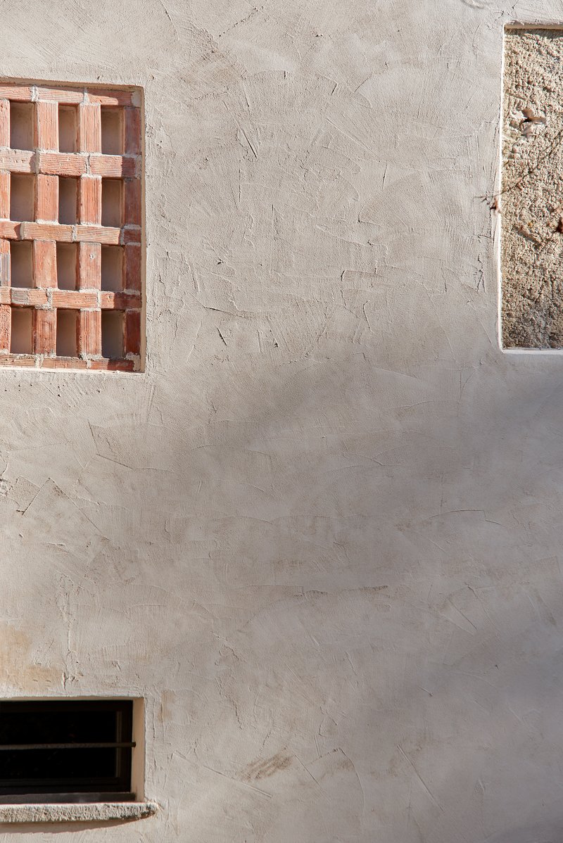 Textured plaster wall with terracotta brick screen window and narrow concrete slit opening