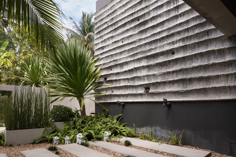 Ribbed concrete wall beside planted beds with palms and gravel under afternoon light