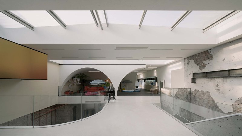 White epoxy floor with curved railing around stair void and arched openings beyond distressed plaster walls