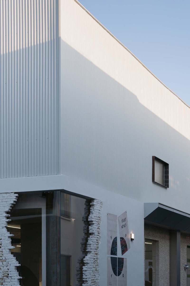 White corrugated metal facade with a cantilevered upper volume and stacked stone entry portal