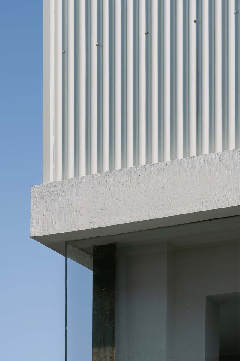 Detail of corrugated cladding meeting a cast concrete edge above a recessed glass opening