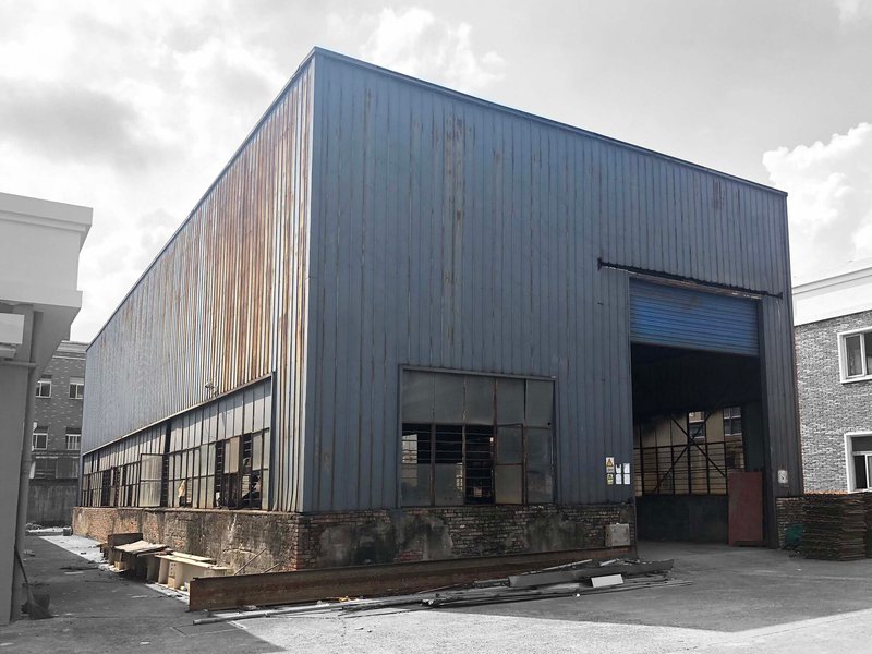 Weathered corrugated metal warehouse with large glazed openings and roll-up door under overcast skies