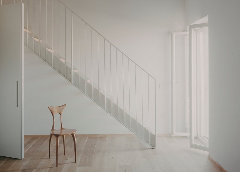 White vertical slatted stair railing with a single wooden chair on light oak flooring