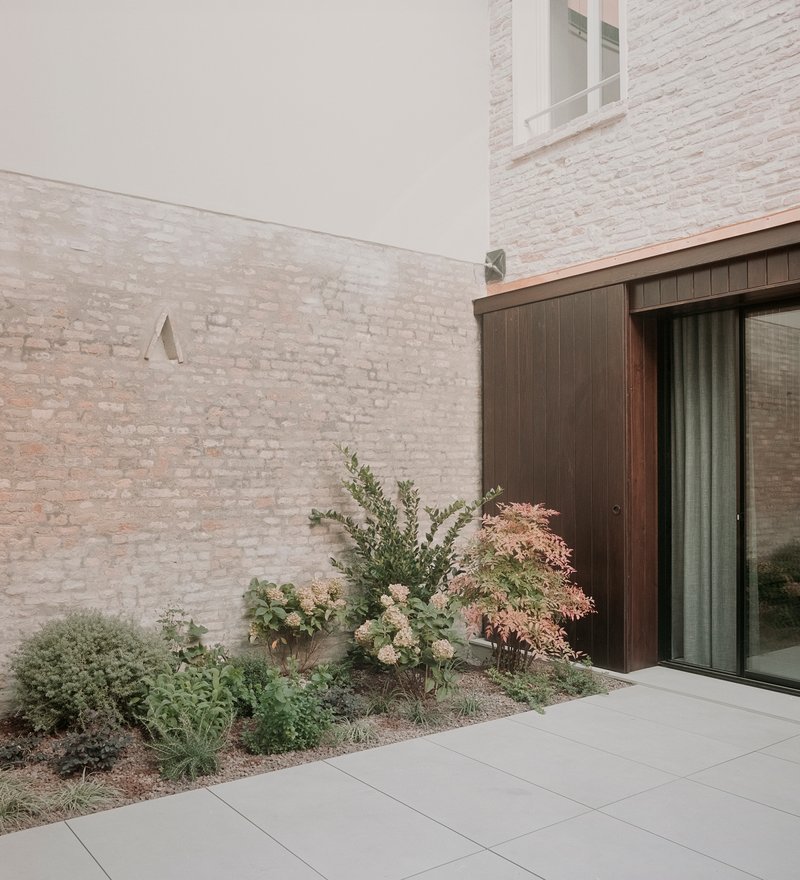Whitewashed brick courtyard wall with a planted bed beside vertical timber cladding and sliding glass door