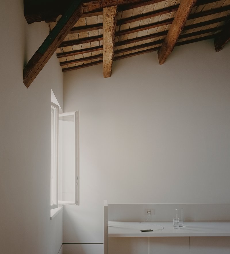 Interior corner with exposed timber beam ceiling and a tall window casting soft afternoon light