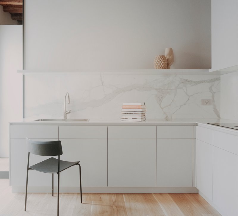 Kitchen counter with white marble backsplash and a single chair on pale wooden flooring