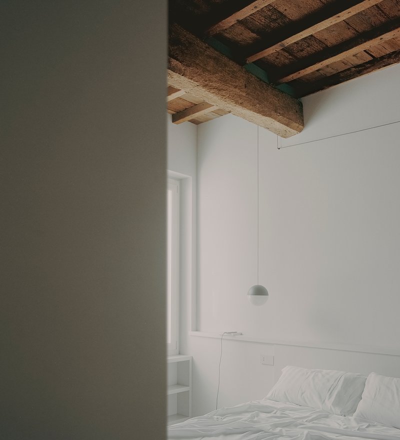 Bedroom view through a doorway showing a pendant light and exposed ceiling beams in soft daylight
