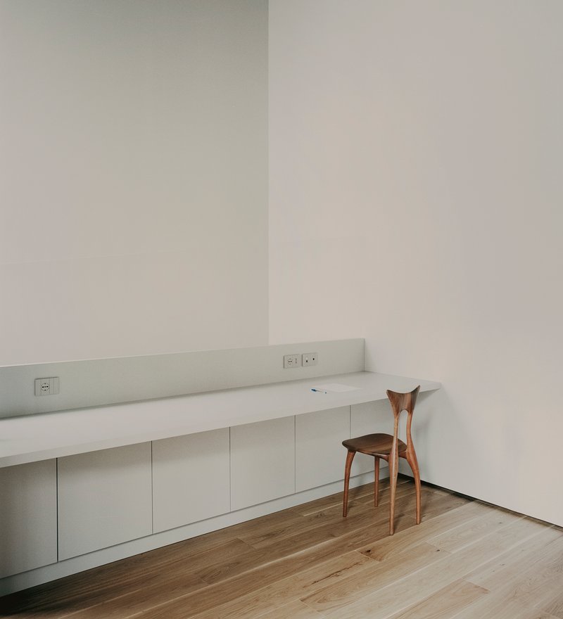 Built-in white desk with integrated electrical outlets and a single wooden chair against pale walls