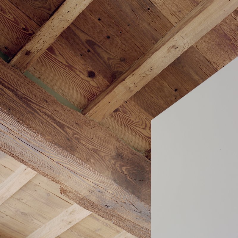 Detail of exposed timber beams and reclaimed wood planks meeting a white painted wall