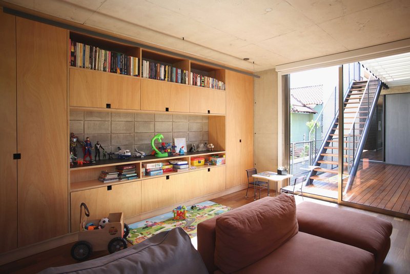 Living room with built-in plywood shelving and open doors framing a timber deck and exterior stair