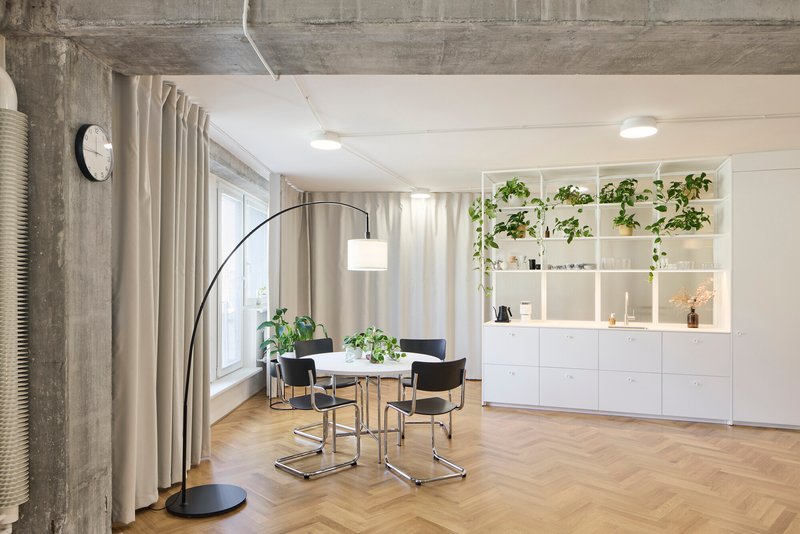 Dining area with exposed concrete ceiling beams and white storage wall lined with potted plants