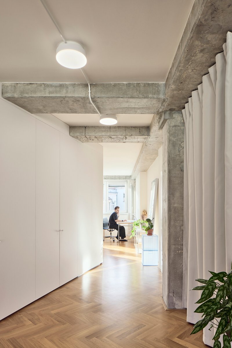 Hallway view showing exposed concrete beams and a figure working at a desk near the window