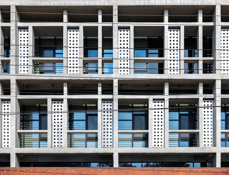 Close-up of the white concrete frame facade showing perforated vertical panels and horizontal floor slabs