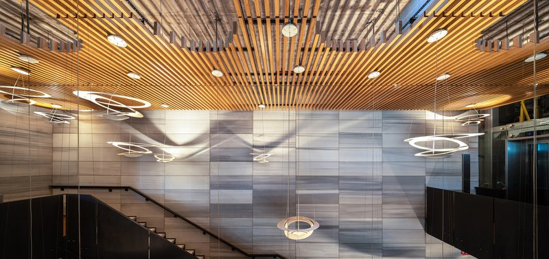 Interior lobby with slatted timber ceiling and circular pendant lights above the striped stone wall