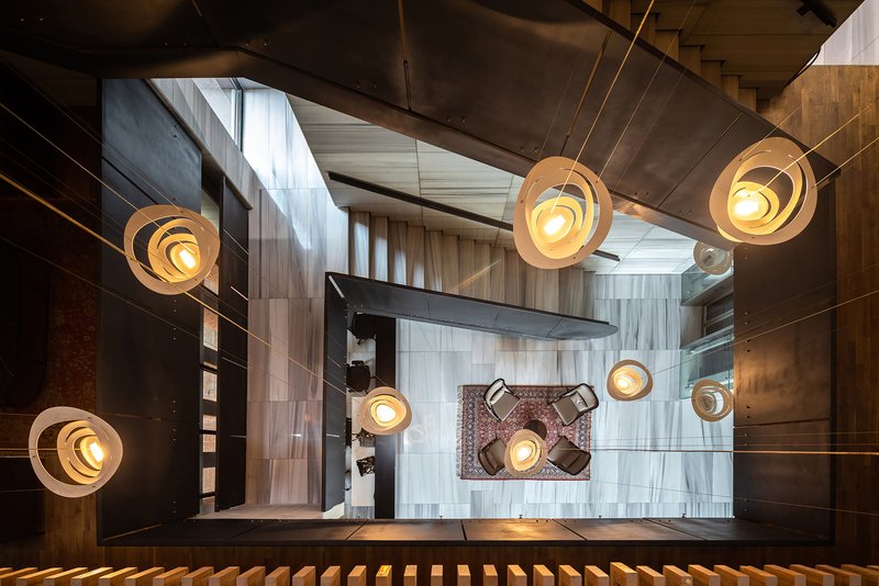 Looking down the stairwell with tiered pendant lights illuminating mixed material walls and tiled floors