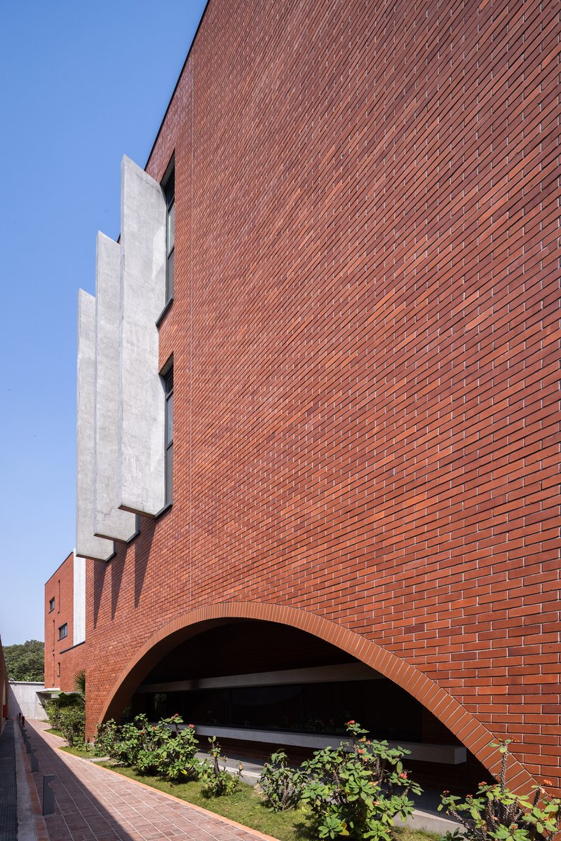 Diagonal brick facade with recessed concrete stairwell and arched opening above landscaped planter beds