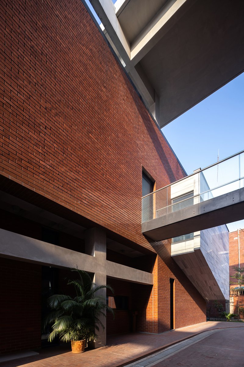 Courtyard entry framed by red brick walls, concrete bridge overhead, and a palm tree in shadow