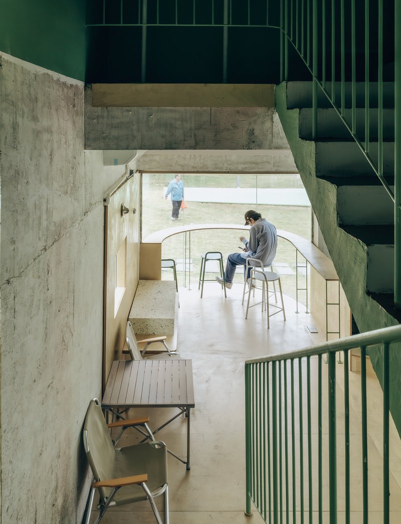 Split-level interior showing concrete walls, green metal staircase, and terrazzo flooring with seated occupants